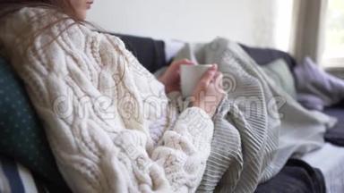 时髦的概念-一个穿白色毛衣的女人手里拿着一杯热咖啡。 女孩躺在沙发上